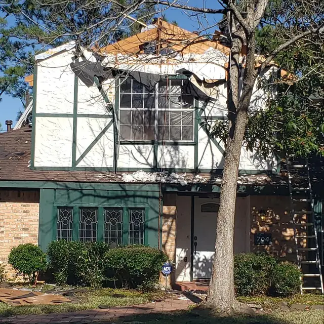 Storm damaged home with siding and roofing torn back, ladder against the wall, mid restoration