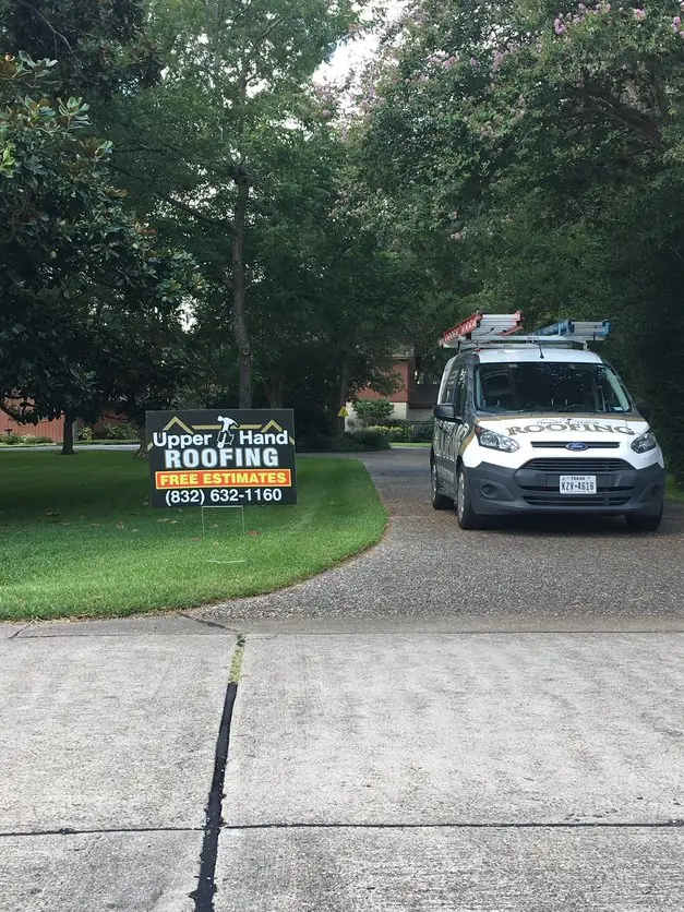 Upper Hand Roofing work van with ladders on the roof rack, parked in a driveway beside the company yard sign
