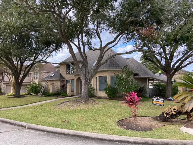 Large brick home with a crew member working on the roof during a project