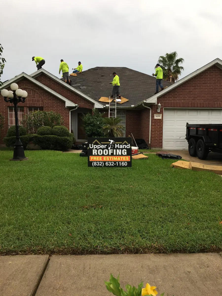 Five person Upper Hand crew in matching high visibility shirts replacing a roof, company trailer in frame